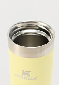 Geel roestvrijstalen beker met een zilveren rand en een glad matte afwerking. Bovenaan de bodem staat het Stanley-logo. De binnenkant is metallic.