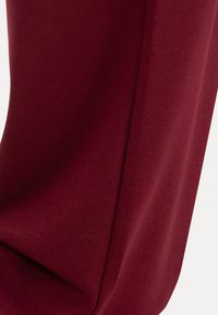 Gros plan d'un tissu bordeaux lisse avec une seule couture verticale et des plis doux.