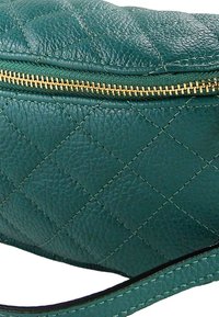 Groene gewatteerde leren tas met een gestructureerd oppervlak, voorzien van een gouden ritssluiting en een zwart bandje. Het ontwerp bevat stiknaden in diamantvorm.