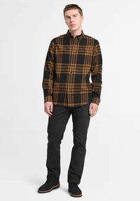 Camicia di flanella a quadri nera e arancione con design a bottoni, maniche lunghe e orlo arrotondato. Abbinata a pantaloni neri e scarpe nere.
