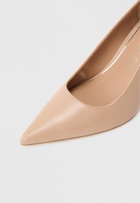 Décolleté beige a punta realizzata in pelle liscia. Presenta un design a taglio basso con una silhouette elegante e dettagli di cuciture sottili.