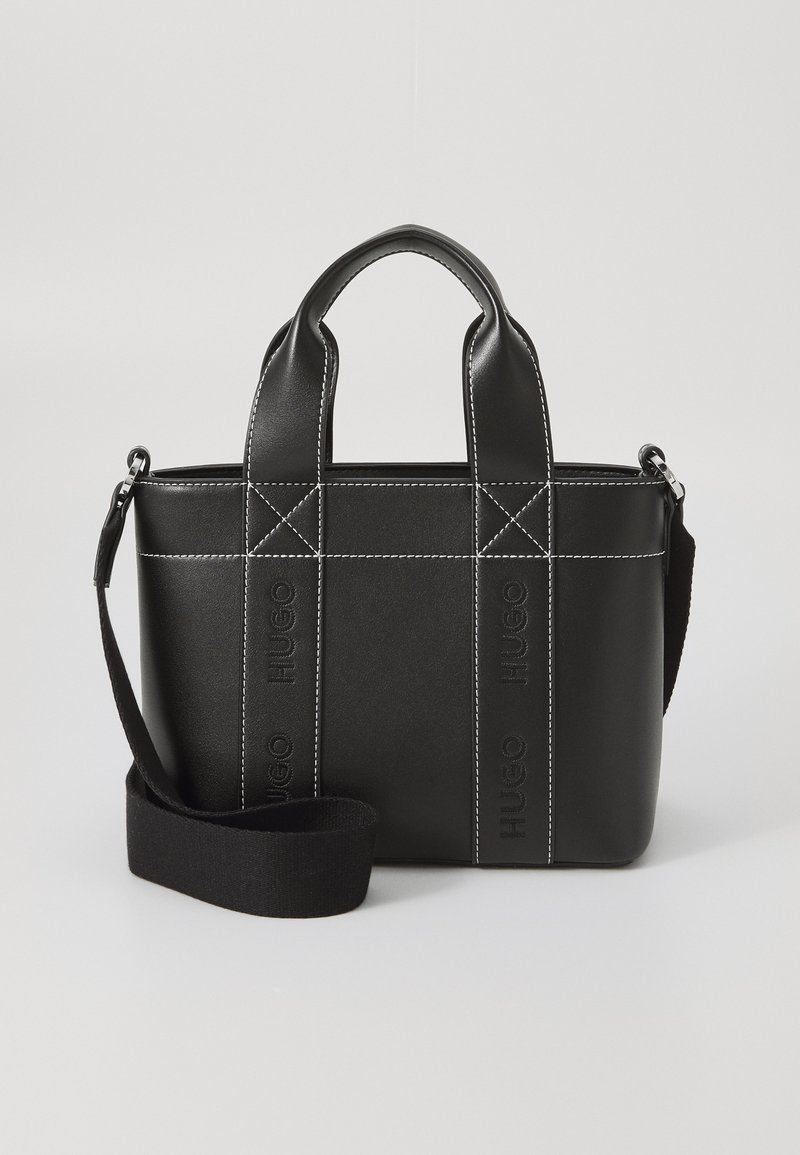 Musta synteettinen käsilaukku, jossa on kaksoiskahvat ja säädettävä hihna. Siinä on kontrastivärinen valkoinen ommel ja kohokuvioitu brändäys sivuilla.