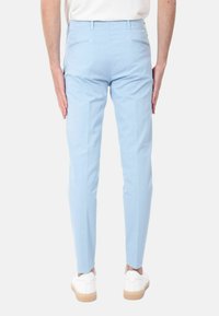 Pantaloni slim-fit azzurro chiaro con una texture liscia, due tasche posteriori con piping, abbinati a sneakers bianche.