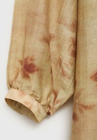 Tessuto leggero di colore beige con motivi tie-dye marrone rossiccio. Presenta una manica a soffietto e una finitura testurizzata.