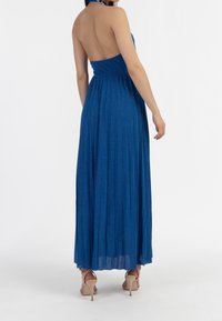 Robe maxi à bretelles bleues avec un corsage ajusté et une jupe plissée fluide. Fabriquée dans un tissu scintillant. Design dos nu et longueur cheville.