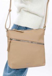 Beige leather crossbody bag with a textured finish, featuring two zippered compartments and a long adjustable strap. Minimalist design.