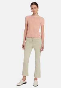 Lichtroze gebreide top met een textuurpatroon, gecombineerd met lichtgroene rechtvaardige jeans. Witte instap sneakers maken de outfit compleet.
