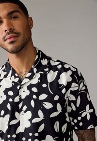 Korte mouwen shirt in zwart en wit met bloemenpatroon, gladde stof, insnoeringkraag en knoopsluiting. Inclusief decoratieve accenten.