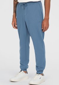 Light blue sweatpants with elastic waistband and drawstring, featuring side pockets and cuffed hems. Pairing white sneakers adds contrast.