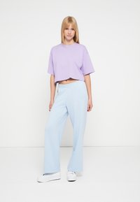 Κοντομάνικη λοβέρ μπλούζα με χαλαρή εφαρμογή, συνδυασμένη με ανοιχτό μπλε παντελόνι με φαρδύ πόδι. Το σύνολο ολοκληρώνουν λευκά αθλητικά παπούτσια.