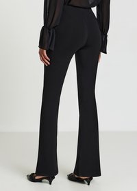 Schwarze ausgestellte Hosen aus glattem Stoff, mit hoher Taille, eng anliegen an den Oberschenkeln und einem sanften Auschnitt von den Knien abwärts.