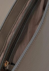 Interno di una borsa in pelle marrone con due scomparti con cerniera, caratterizzato da una fodera liscia con strisce sottili e un marchio in rilievo.