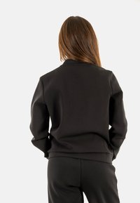 Felpa nera con collo a giro, maniche lunghe e vestibilità rilassata. Tessuto liscio, design minimale e senza loghi o motivi visibili.