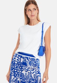 White cotton t-shirt with short sleeves, paired with a blue patterned skirt featuring abstract designs and a blue crossbody bag.