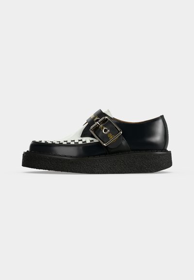 Mocassin en cuir noir et blanc avec détail tissé à l'avant, semelle noire épaisse et large bride à boucle argentée sur le dessus.
