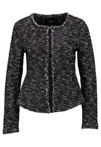 Veste texturée noir et blanc avec un col rond, des manches longues et un bord à franges le long de la fermeture, présentant une silhouette cintrée.