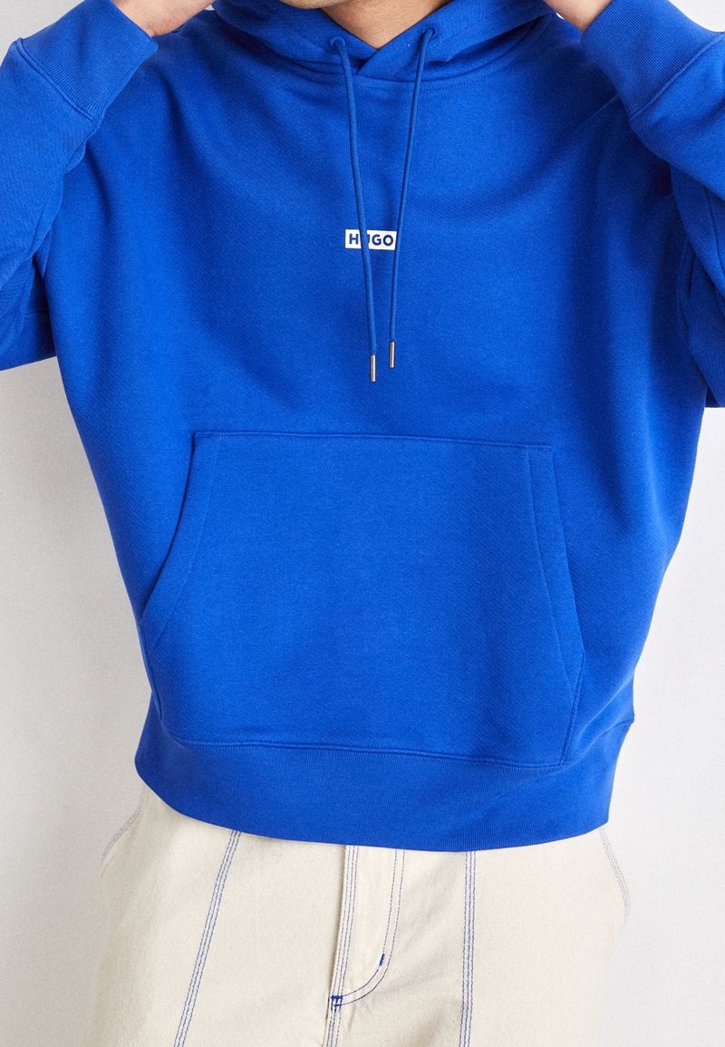 Felpa blu con tasca frontale, cappuccio regolabile e piccolo logo sul petto. Il materiale è morbido, di un colore uniforme e ha una vestibilità comoda.