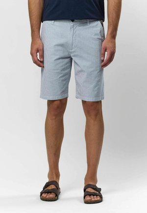 Világoskék csíkos szoknya, lapos elülső résszel, oldalzsebekkel és felgöngyölt szegéllyel. Barna szandálokkal viselve mezítláb. Texturált anyag.