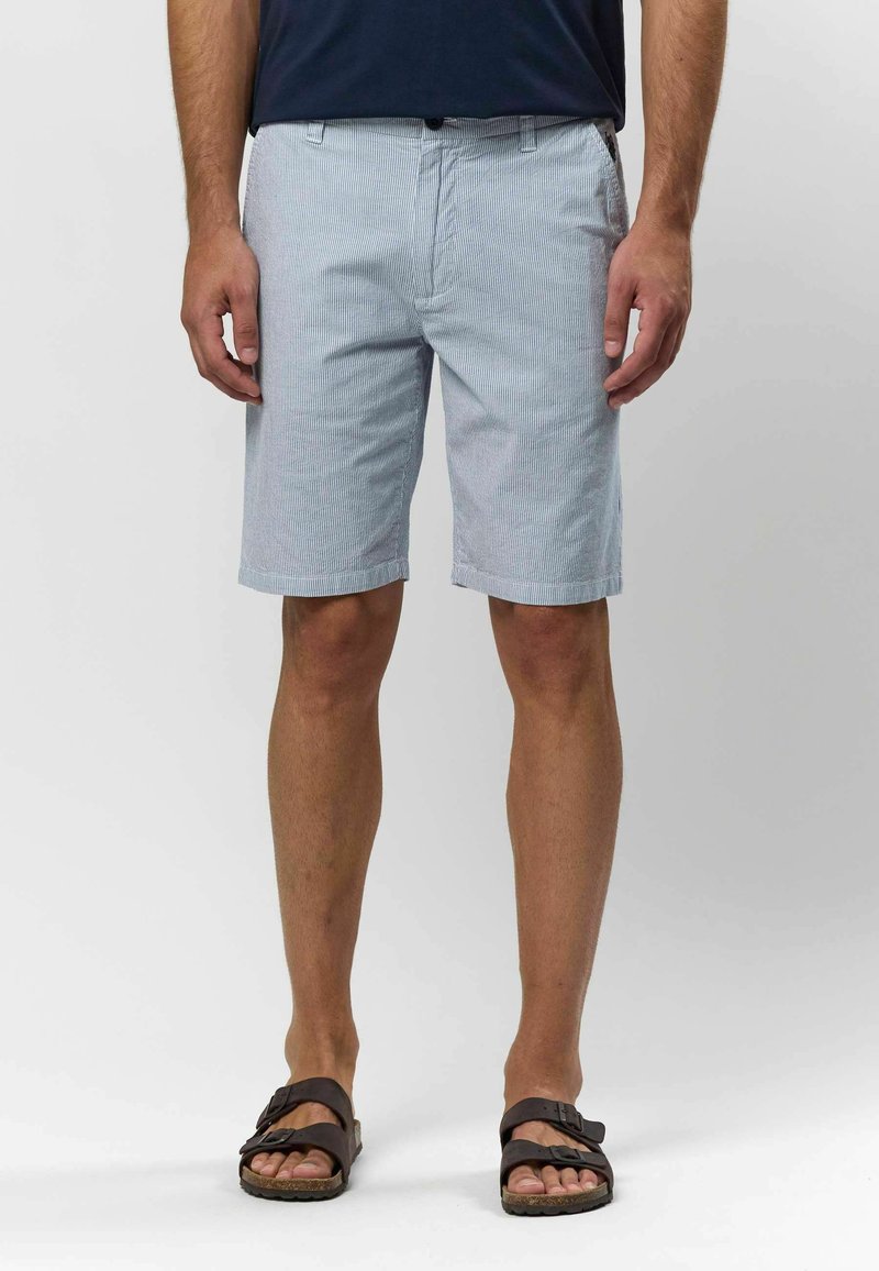 Shorts bleu clair à rayures avec un devant plat, des poches latérales et un ourlet replié. Portés avec des sandales marron sur pieds nus. Tissu texturé.