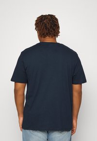 Mornarji moder bombažni T-shirt, kratki rokavi, krožni izrez, sproščen kroj, mehak material, brez vidnih vzorcev ali logotipov. Pogled zadaj.