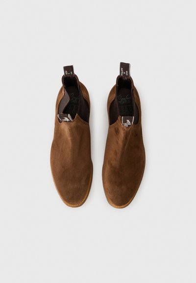 Pantofi slip-on din suede maro, cu o textură netedă, vârf rotunjit, panouri laterale elastice și o talpă din cauciuc maro contrastant.