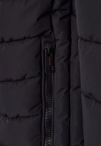 Giubbino nero imbottito con sezioni trapuntate, dotato di una zip laterale in un design nero e arancione, texture liscia e costruzione compatta.