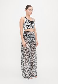 Top corto floreale in bianco e nero con spalline sottili abbinato a pantaloni ampi trasparenti neri floreali, dotati di vita alta e motivi delicati.