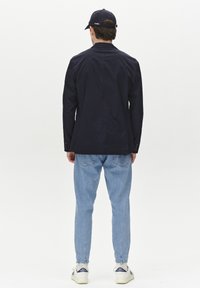 Chaqueta de algodón navy con corte recto, combinada con pantalones de mezclilla azul claro, zapatillas blancas con acentos azules y una gorra navy.