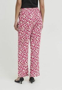 Wijdvallende broek met bloemenpatroon in het wit, met roze en groene bloemen. Elastische tailleband en vloeiende stof met een zachte textuur.