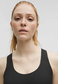 Black athletic tank top with wide straps, round neckline, smooth texture, and minimal stitching details. Model displays close-up view.