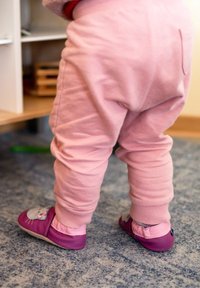 Rosa Sweatpants mit elastischen Bündchen, kombiniert mit lila Slippers mit einem Katzenkopfdesign und pinken Akzenten. Weicher, texturierter Stoff.