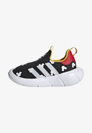 Sneaker noir sans lacets avec motifs de tête de Mickey Mouse blancs, trois bandes blanches sur le côté, doublure jaune, languette de talon rouge et semelle blanche épaisse.