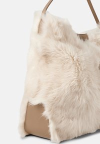 Tragetasche mit cremefarbenem Kunstfell außen und beigem Lederboden. Verfügt über eine weiche, flauschige Textur und glatte Lederakzente.