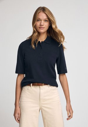 Polo shirt bleu marine avec un col classique, des manches courtes, une patte de boutonnage à trois boutons et une coupe décontractée, associé à un pantalon beige et une ceinture marron.