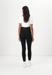 Black high-waisted pants with a textured design, two back pockets, and a snug fit, paired with a white top featuring scalloped sleeves.