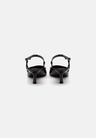 Ζευγάρι μαύρες γόβες slingback από δερμάτινο λουστρίνι με μέτριου ύψους κωνικά τακούνια και λουράκια στο λαιμό του ποδιού με μικρές χρυσές αγκράφες, εμφανίζονται από πίσω.