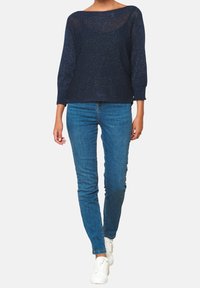 Marineblau gestrickter Pullover mit lockerer Passform, langen Ärmeln und weitem Halsausschnitt. Kombiniert mit enganliegenden blauen Jeans und weißen Sneakers.