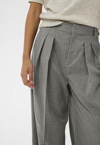 Szare spodnie w prążki z zakładkami, dopasowany krój, lekką tkaninę i gładką fakturę. Posiadają pas z ukrytymi zapięciami.