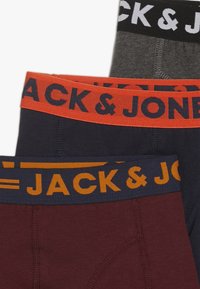 Tričko s elastickým pásom, ktoré obsahuje tri páry boxeriek. Farby: čierna, šedá a tmavočervená. Každý pás je označený textom 'JACK & JONES' v kontrastných farbách.