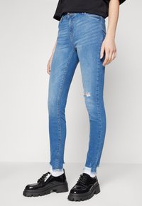 Visokotemne modre skinny kavbojke z raztrganim kolenom, strganim robom in gladko denim teksturo, v kombinaciji z črnimi platformnimi čevlji.