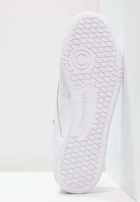 Bílá podrážka tenisek Reebok s diamantovým vzorem, detailní obvodová struktura pro lepší grip a vyražené logo "Reebok", vyfoceno na bílem pozadí.
