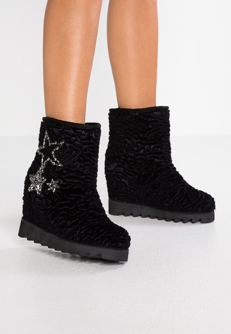 Botas de tobillo de cuña negras con textura, suelas dentadas y tres adornos en forma de estrella plateada en el lado exterior de la bota izquierda.
