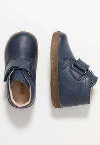 Scarpe in pelle blu navy con punta arrotondata, cinturino in velcro e suola marrone testurizzata. Finitura liscia con dettagli di cucitura e rivestimento interno.