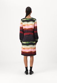 Kleid z zloženimi večbarvnimi vodoravnimi črtami v rdeči, zeleni, roza in rjavi barvi. Narejeno iz gladkega blaga z dolgimi rokavi in okroglimi izrezom.