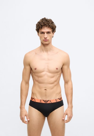 Cuecas boxer masculinas pretas com cintura estampada com logótipo laranja. O tecido parece suave, ajustando-se ao corpo de forma confortável e realçando a forma contornada.