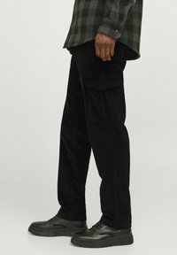 Sorte kordfløjspants med sidelommer, der har en lige pasform og tekstureret stof, parret med sorte snørebåndssko.