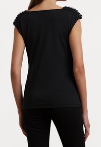 Svart kortärmad topp med kvadratisk halsringning och dekorativa axel detaljer. Mjuk, elastisk tyg med en slät yta.