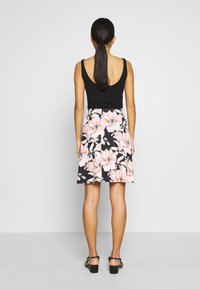 Zwarte tanktop met een lage rug, gecombineerd met een knie-lange rok met een bloemenpatroon in roze en blauw op een zwarte achtergrond.