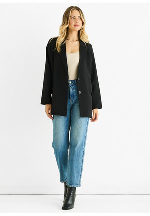 Black blazer with two buttons and pockets, worn over a beige top, paired with loose blue jeans and black ankle boots.