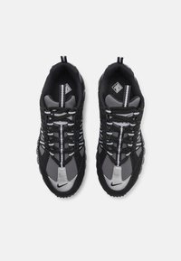 Adidași negri și gri cu un superior din plasă texturată, accente reflective și o talpă amortizantă. Prezintă șireturi groase și un design geometric.